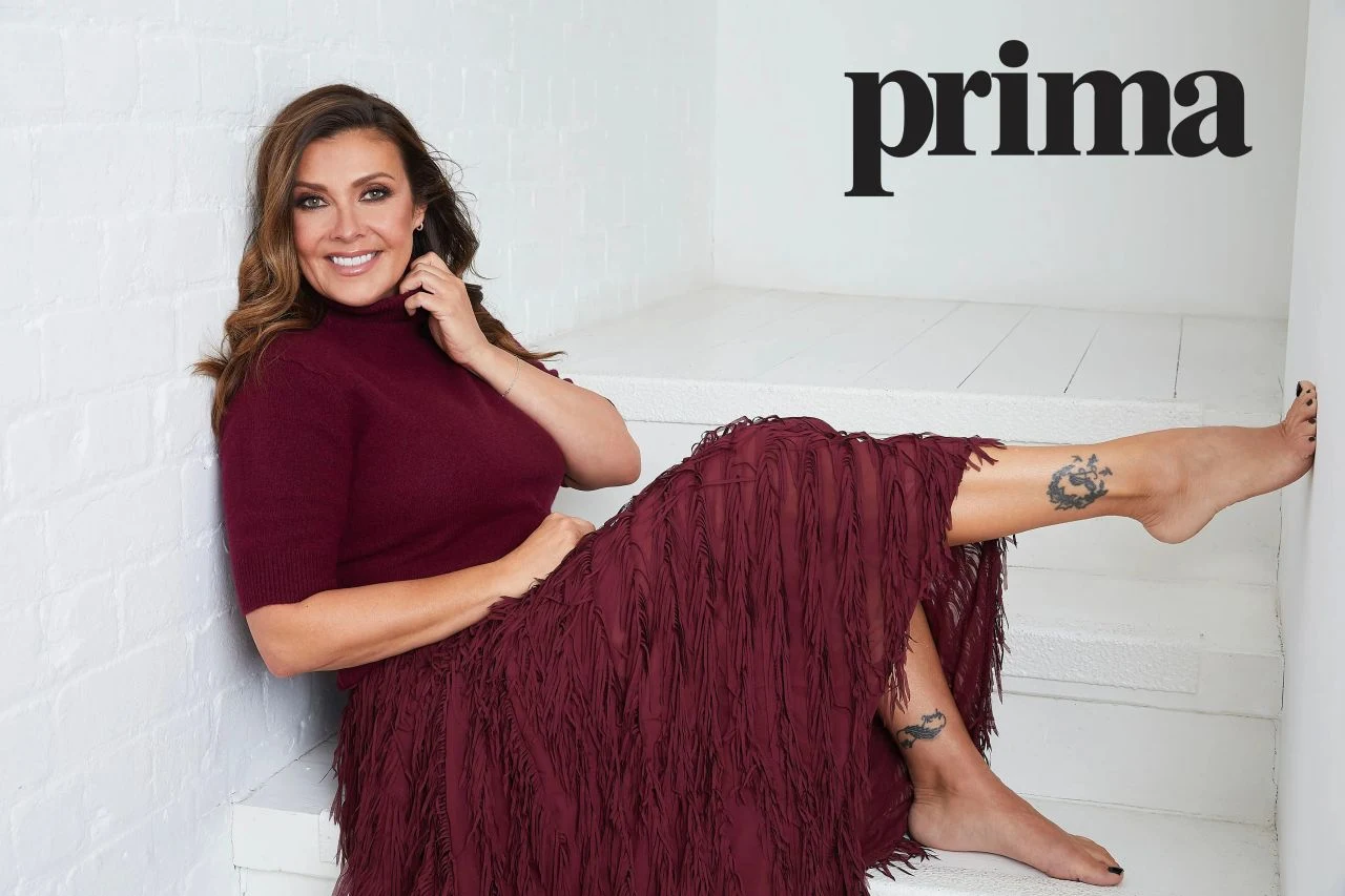Kym Marsh barefoot in a burgundy top and fringed skirt for Prima UK February 2026