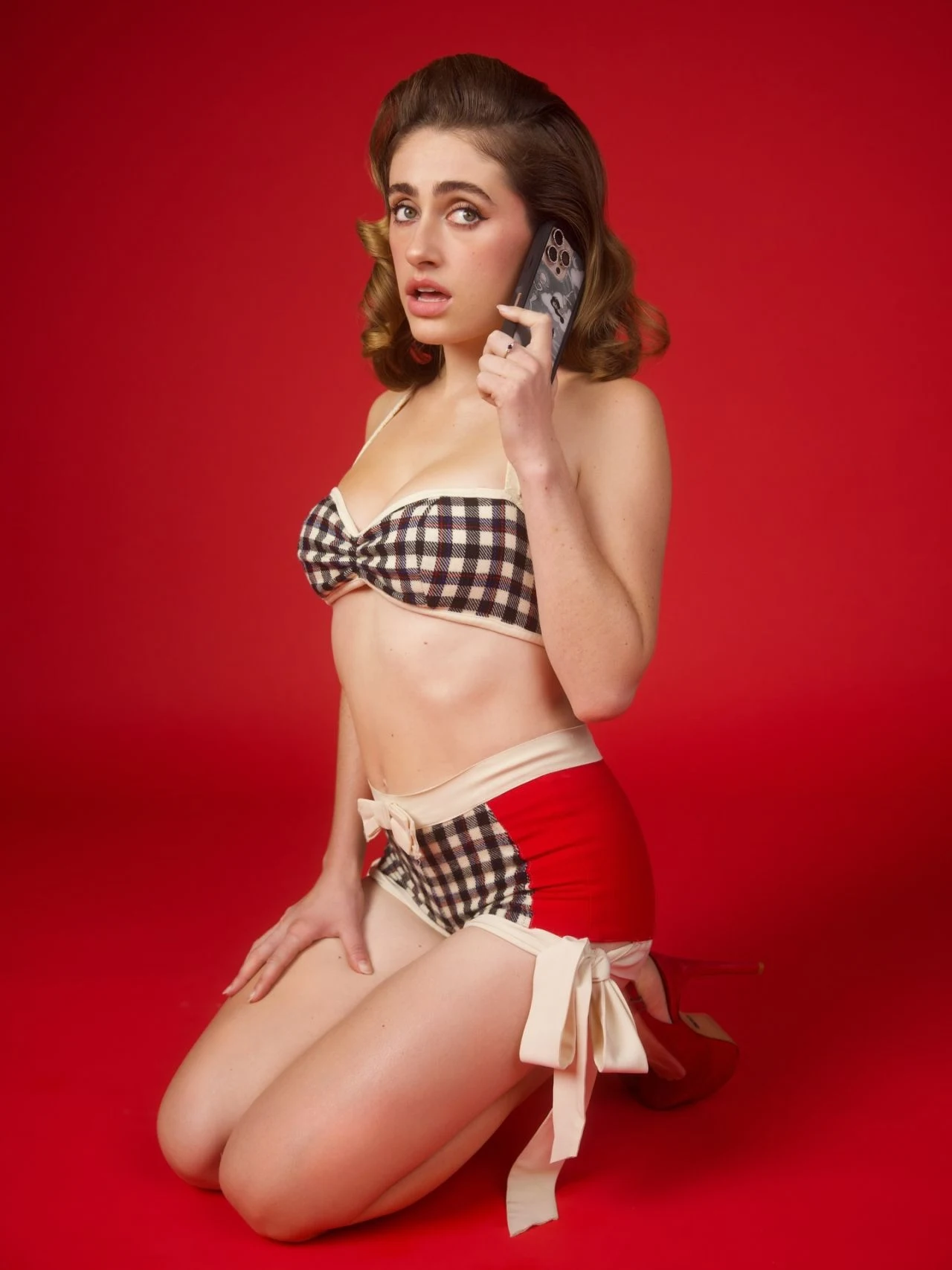 Rachel Sennott kneeling on a red floor wearing a checkered bikini top for Wildflower Cases campaign