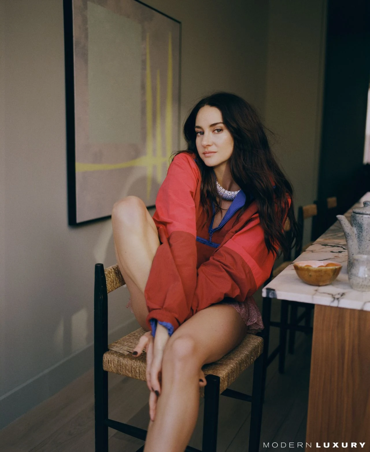 Shailene Woodley relaxed in a woven chair wearing a stylish red and blue jacket