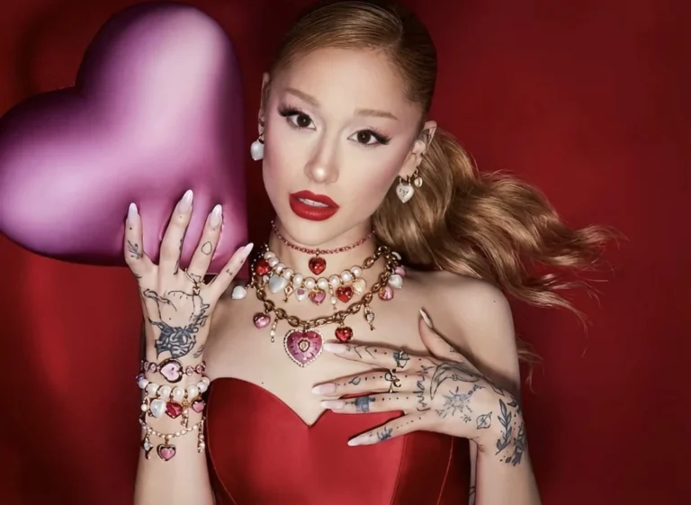 Ariana Grande reclining in red satin with layered Swarovski heart necklaces and pearl earrings