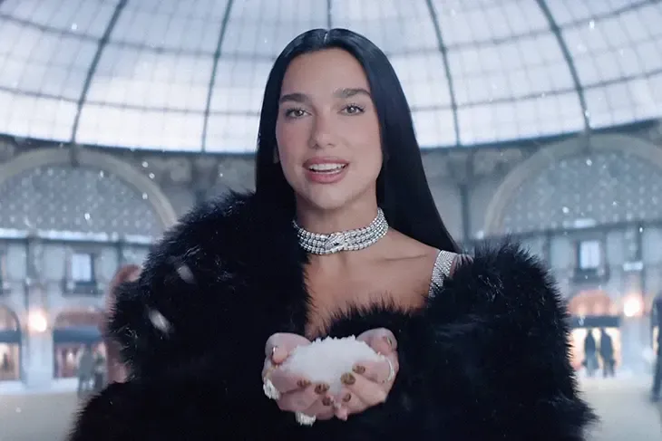 Dua Lipa wearing black fur coat inside Milan’s Galleria for NBC Olympics promo