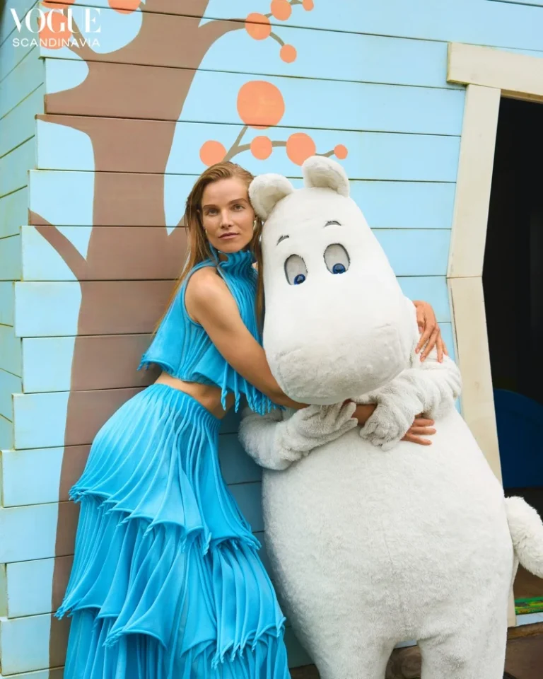 Suvi Riggs Koponen posing with the Moomin outside a pastel-blue cottage for Vogue Scandinavia